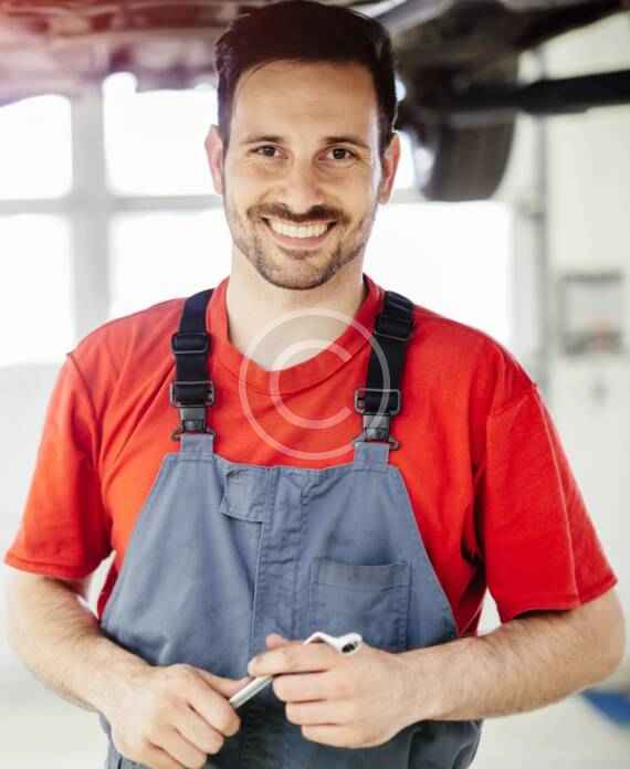 Smiling man in red shirt and gray apron with glasses hanging around his neck.