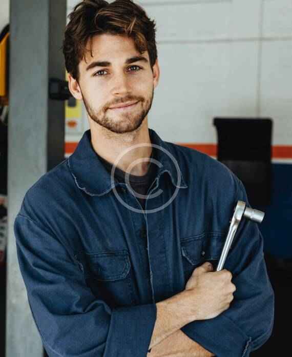 Young mechanic holding wrenches and smiling confidently.