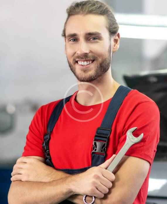Smiling mechanic in red shirt holding a wrench.