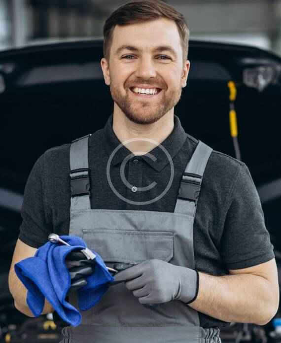 Smiling mechanic holding blue gloves in a workshop.